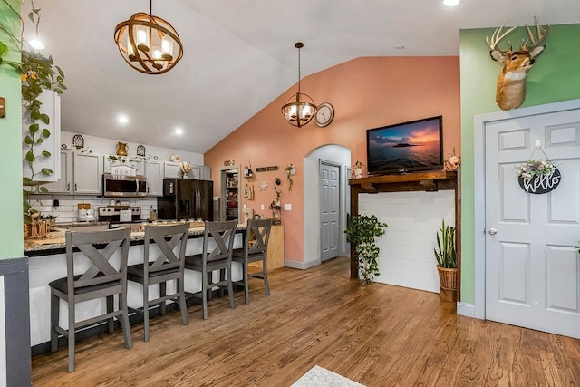 kitchen with lofted ceiling, decorative light fixtures, light hardwood / wood-style floors, and black refrigerator with ice dispenser