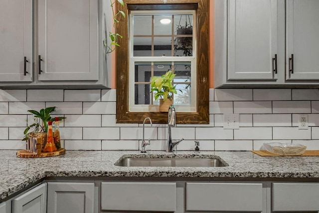 kitchen with light stone countertops, sink, and backsplash