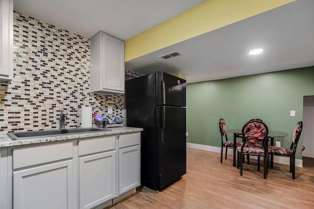 kitchen with sink, black refrigerator, white cabinetry, decorative backsplash, and light wood-type flooring