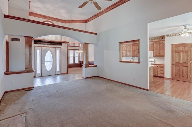 foyer entrance featuring decorative columns, a towering ceiling, light carpet, and ceiling fan