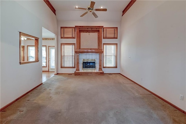 unfurnished living room with light carpet, a tiled fireplace, ceiling fan, and a high ceiling