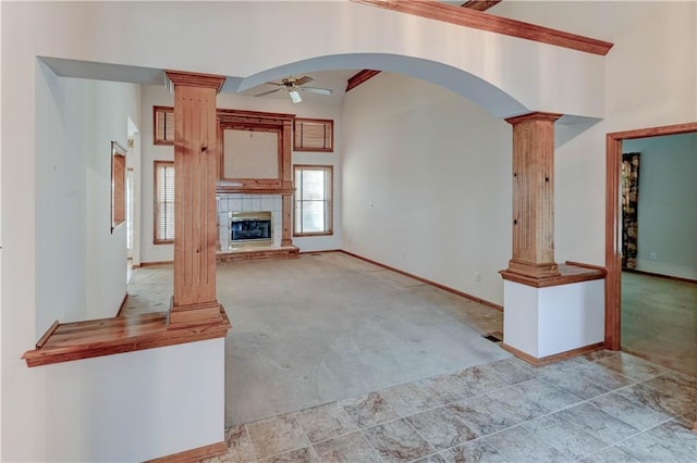 unfurnished living room featuring ornate columns, a tile fireplace, a towering ceiling, ceiling fan, and light carpet