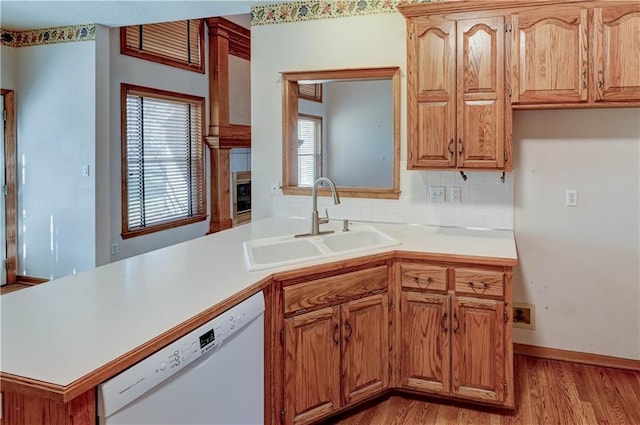 kitchen with tasteful backsplash, dishwasher, sink, kitchen peninsula, and light wood-type flooring