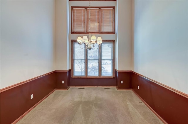 spare room featuring an inviting chandelier, light carpet, and wood walls