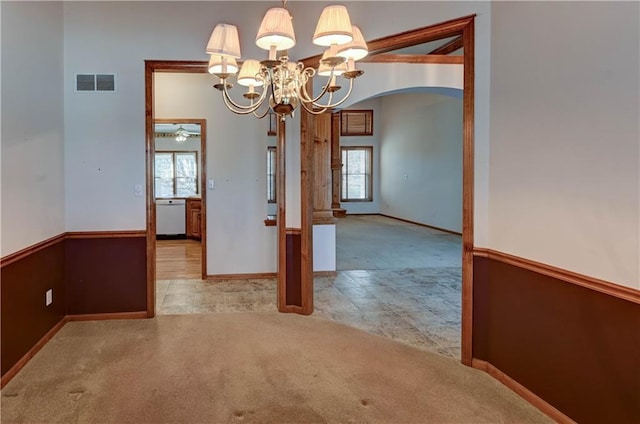 unfurnished dining area with ceiling fan with notable chandelier, a wealth of natural light, and light colored carpet