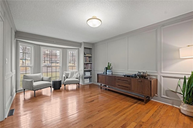 sitting room with built in shelves, a textured ceiling, and light hardwood / wood-style flooring