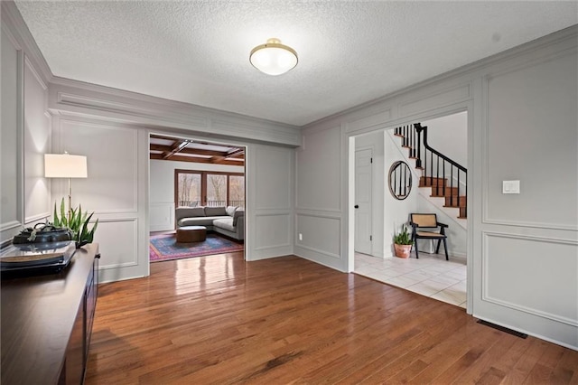 entryway with crown molding, beam ceiling, light hardwood / wood-style flooring, and a textured ceiling