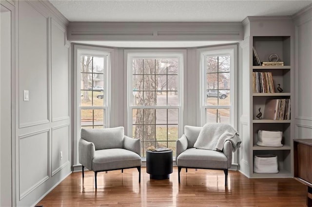 living area with hardwood / wood-style flooring, crown molding, a textured ceiling, and built in shelves