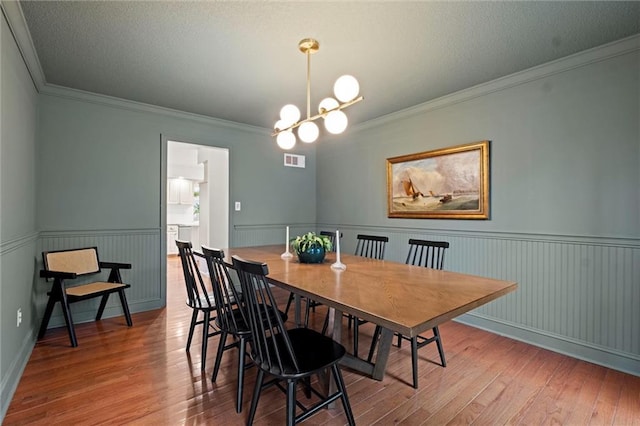 dining area with wood-type flooring, ornamental molding, a textured ceiling, and an inviting chandelier