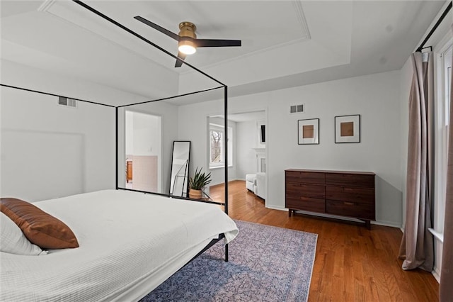 bedroom with hardwood / wood-style flooring, ceiling fan, and a raised ceiling