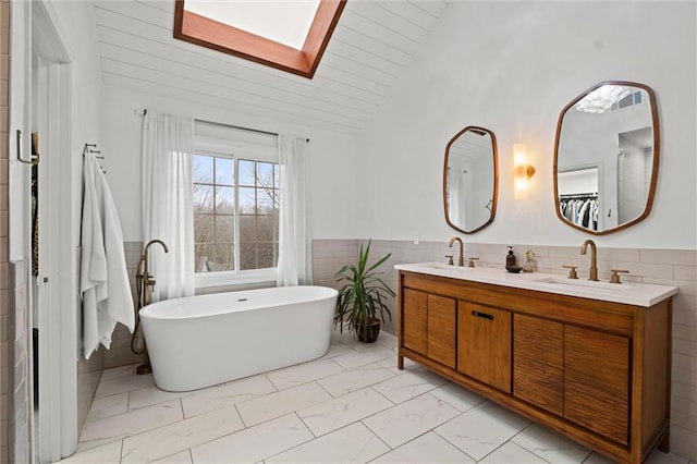 bathroom featuring a bathing tub, lofted ceiling with skylight, tile walls, and vanity