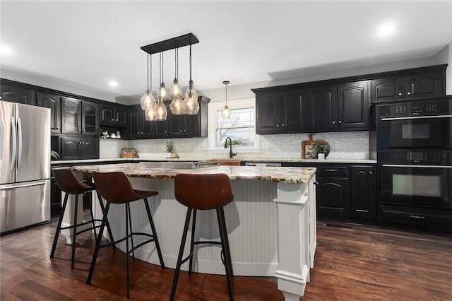 kitchen featuring dark wood-type flooring, a center island, hanging light fixtures, stainless steel fridge, and double oven