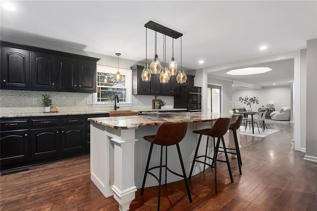 kitchen featuring decorative light fixtures, dark wood-type flooring, light stone countertops, and a kitchen island