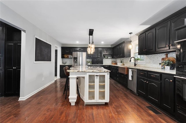 kitchen with a kitchen island, decorative light fixtures, backsplash, stainless steel appliances, and light stone countertops