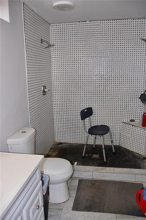 bathroom with a tile shower, vanity, and toilet