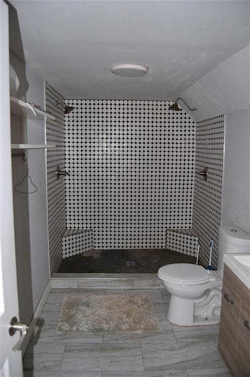 bathroom with vanity, lofted ceiling, tiled shower, and toilet