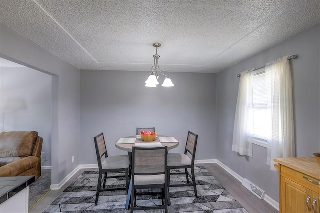 dining area with a chandelier, a textured ceiling, dark wood-style flooring, visible vents, and baseboards