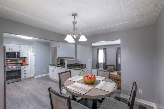 dining space with a textured ceiling, wood finished floors, visible vents, baseboards, and an inviting chandelier