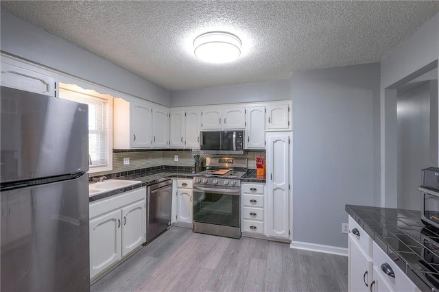 kitchen featuring appliances with stainless steel finishes, light wood-type flooring, white cabinets, and decorative backsplash