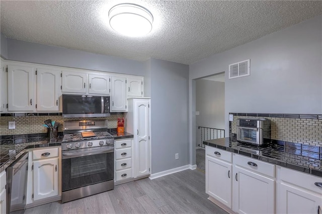 kitchen featuring appliances with stainless steel finishes, white cabinets, visible vents, and light wood finished floors