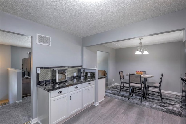 kitchen with a notable chandelier, visible vents, white cabinets, tasteful backsplash, and dark wood finished floors