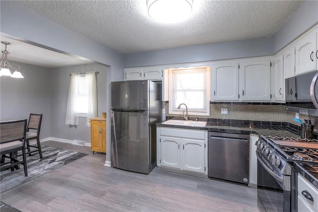 kitchen with gas range oven, freestanding refrigerator, white cabinetry, a sink, and dishwasher