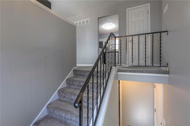 stairway with baseboards, visible vents, and a textured ceiling