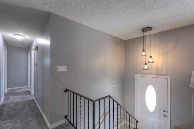 foyer entrance with carpet flooring, a textured ceiling, and baseboards