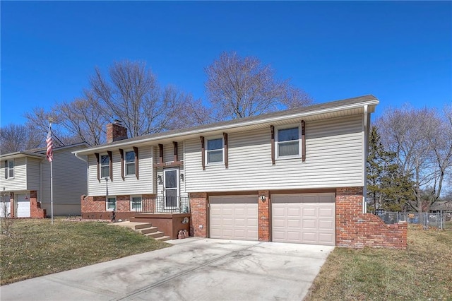 raised ranch with driveway, a chimney, an attached garage, a front lawn, and brick siding