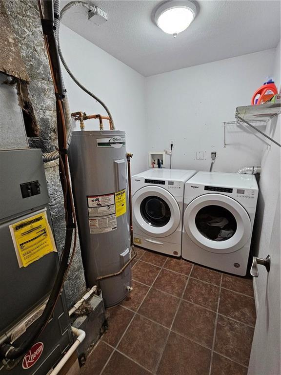 washroom featuring dark tile patterned flooring, washing machine and dryer, water heater, and a textured ceiling