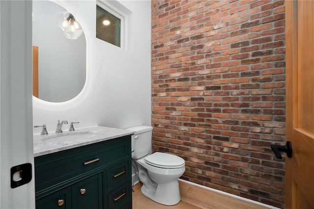 bathroom with brick wall, vanity, and toilet