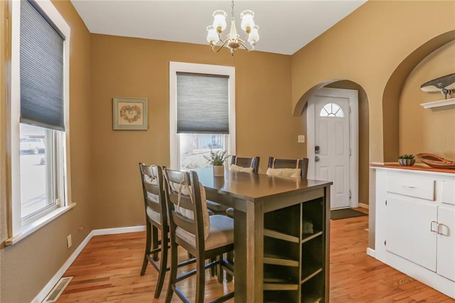 dining space featuring light wood finished floors, visible vents, baseboards, arched walkways, and a notable chandelier