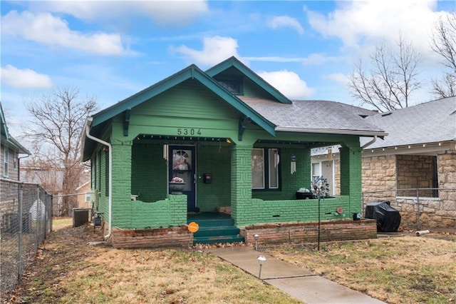 bungalow with brick siding, covered porch, a shingled roof, and fence