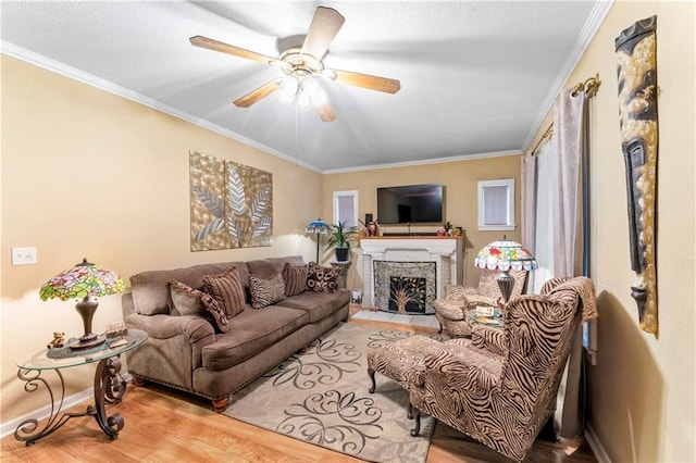 living room with wood finished floors, a ceiling fan, a fireplace with flush hearth, ornamental molding, and a textured ceiling