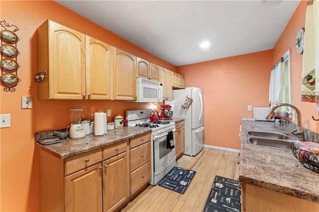 kitchen featuring baseboards, light brown cabinetry, light wood-style floors, white appliances, and a sink