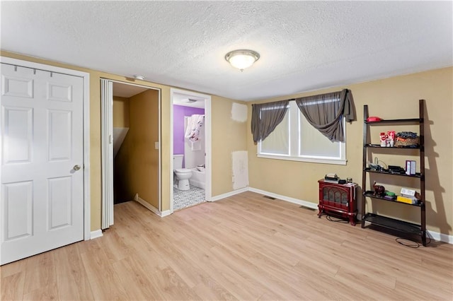 unfurnished bedroom with baseboards, connected bathroom, a textured ceiling, and light wood-style floors