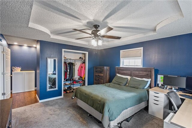 bedroom featuring dark carpet, a tray ceiling, a closet, and a textured ceiling