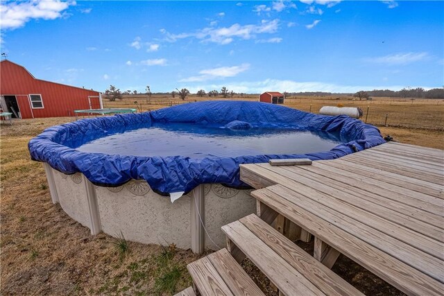 view of swimming pool with an outbuilding, a wooden deck, and a rural view