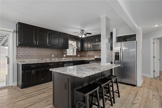 kitchen featuring a kitchen island, a breakfast bar area, stainless steel appliances, light stone countertops, and light wood-type flooring