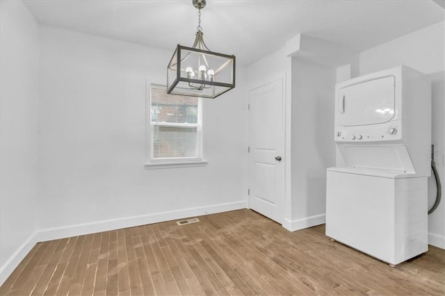 clothes washing area featuring a notable chandelier, wood-type flooring, and stacked washer / dryer