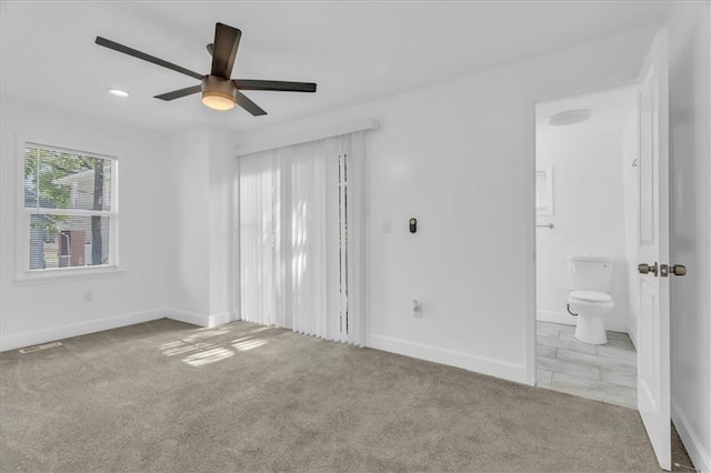 interior space with ensuite bath, light colored carpet, and ceiling fan