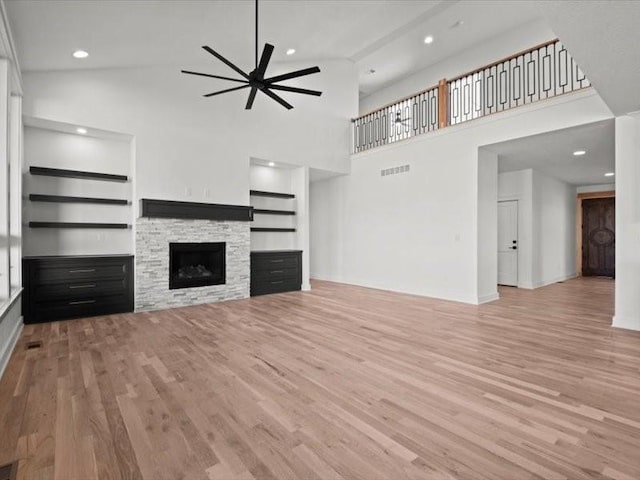 unfurnished living room with ceiling fan, built in shelves, a stone fireplace, visible vents, and light wood finished floors