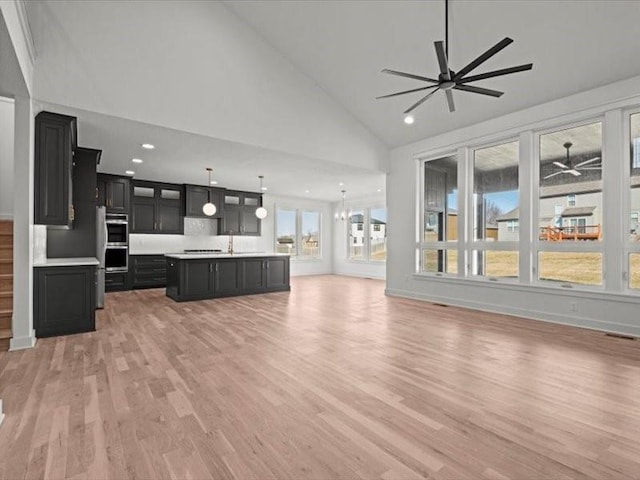 unfurnished living room featuring light wood finished floors, visible vents, high vaulted ceiling, a sink, and ceiling fan with notable chandelier