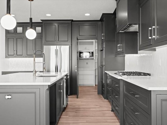 kitchen featuring a center island with sink, light countertops, backsplash, light wood-type flooring, and wall chimney exhaust hood