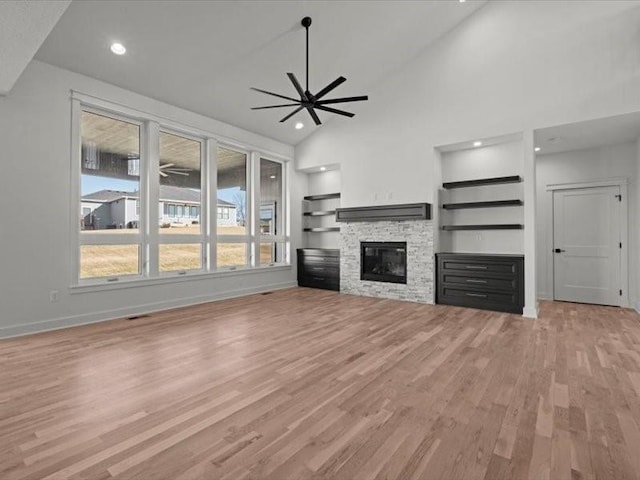 unfurnished living room with light wood-style floors, ceiling fan, a stone fireplace, and baseboards