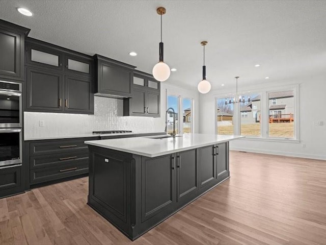 kitchen with a center island with sink, light countertops, stainless steel double oven, light wood-type flooring, and a sink