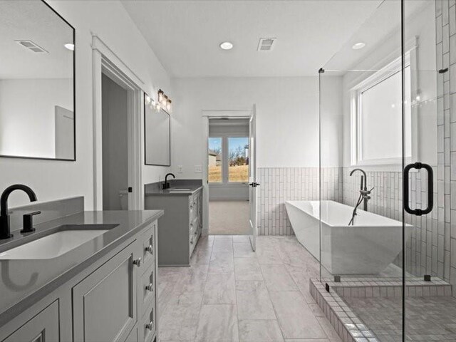 bathroom featuring two vanities, a freestanding tub, visible vents, and a sink