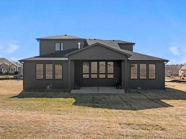 rear view of property with a shingled roof, a lawn, and a patio area