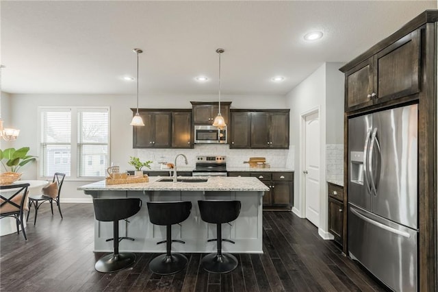 kitchen with dark wood finished floors, stainless steel appliances, backsplash, a sink, and dark brown cabinets