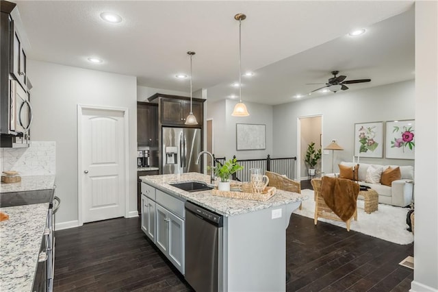 kitchen featuring light stone counters, stainless steel appliances, a sink, open floor plan, and dark wood-style floors